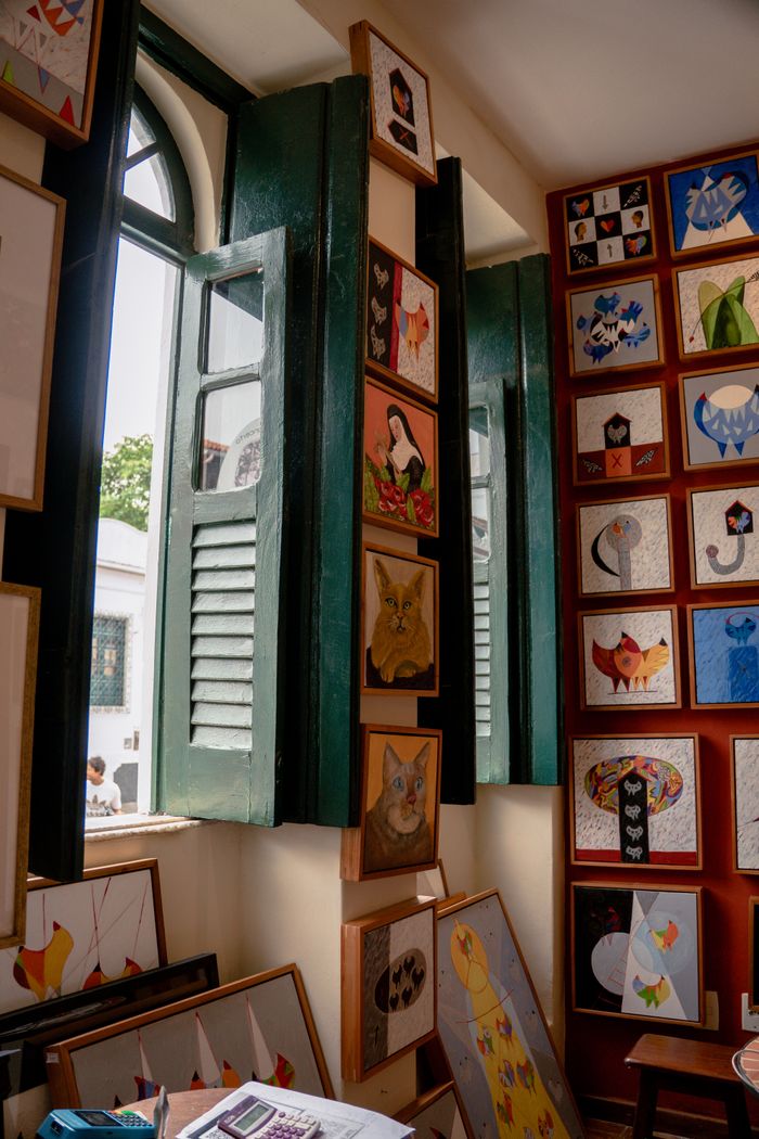 Cozy indoor art gallery featuring colorful paintings and green shuttered windows.